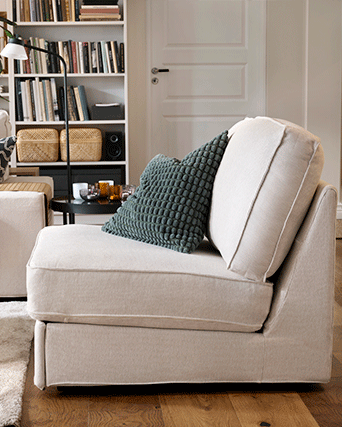Cojín verde con relieve sobre un sillón beige en una estancia acogedora con librería y puerta blanca.