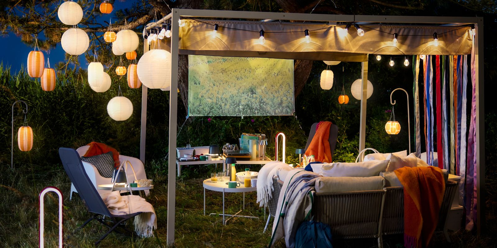 Cozy outdoor terrace with HAMMARÖN pergola and SEGERÖN outdoor sofa, lit by hanging SOLVINDEN lamps.