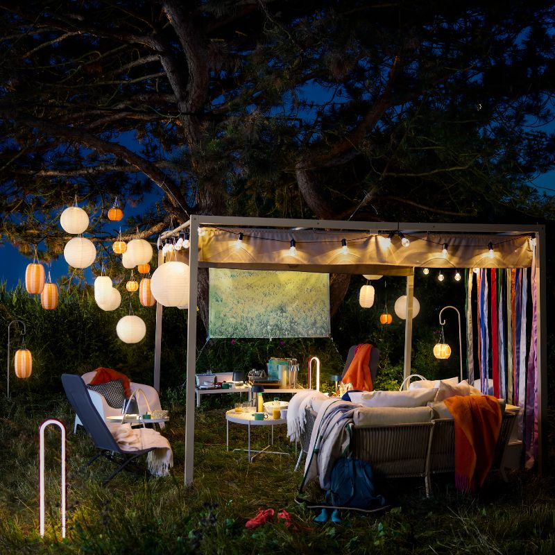 Cozy outdoor terrace with HAMMARÖN pergola and SEGERÖN outdoor sofa, lit by hanging SOLVINDEN lamps.