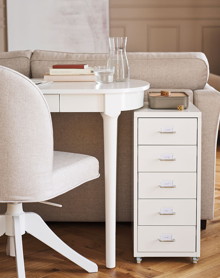 A ROSENTORP swivel chair and a white HELMER drawer unit on castors stand at a white ROSENTORP desk behind a sofa.