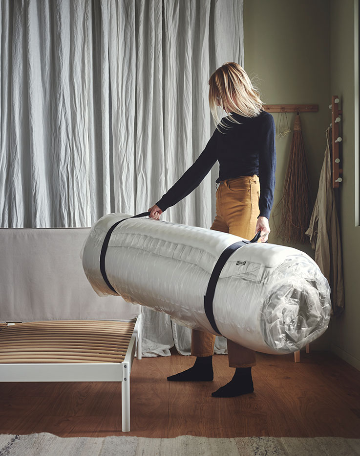 Mujer sujetando un fardo con un colchóenrollado listo para colocar en la cama