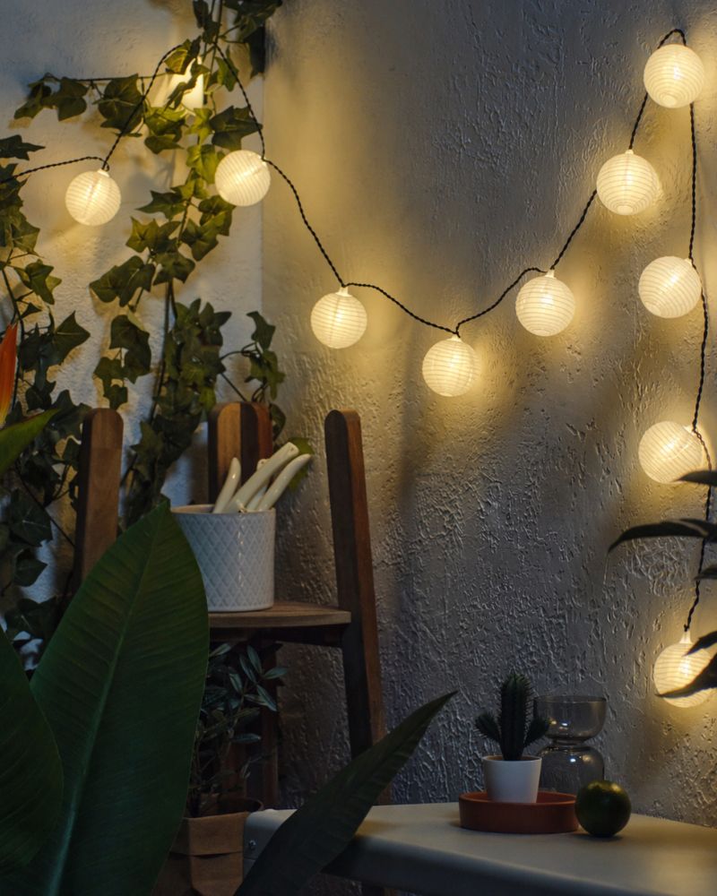 Cozy patio corner with IKEA SOLVINDEN LED light chains and FEJKA artificial potted plant adding warm ambient charm.