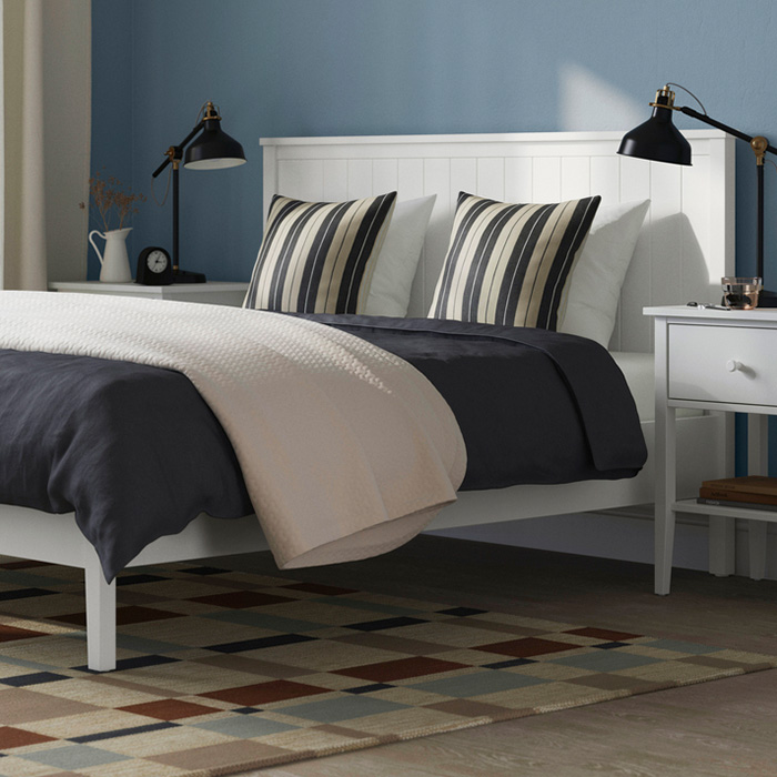 A modern bedroom featuring a white bed, striped pillows, black lamps, and a multi-colored geometric rug.