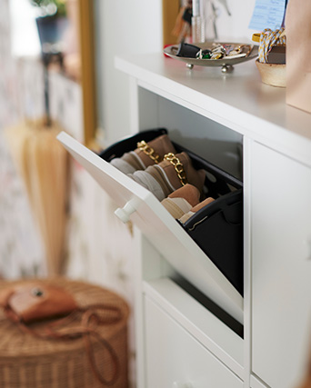 White shoe cabinet open with beige shoes inside, on a wicker floor and bright decoration.
