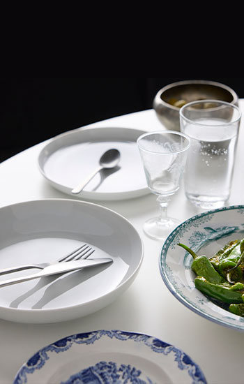 Part of a table set for a meal, with PRAKTBOTIA cutlery, an IKEA 365+ deep plate, an IKEA 365+ side plate, glasses and food.