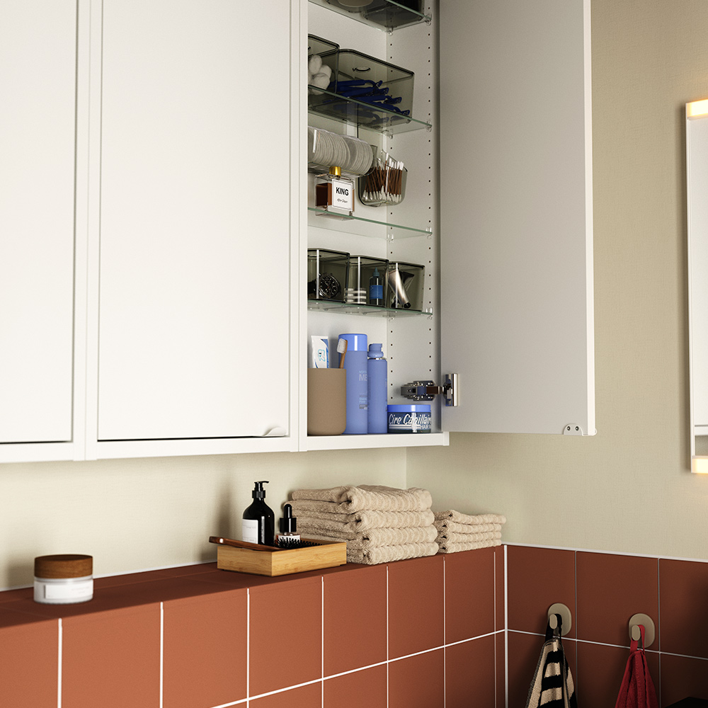 A terracotta-tiled bathroom featuring a white HAVBÄCK wall cabinet, one door open to show glass shelves storing toiletries.