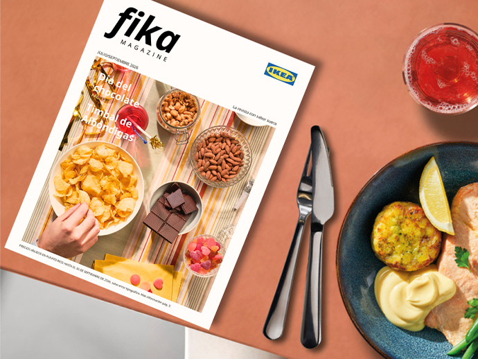 Front cover of IKEA's "Fika Magazine" placed on a terracotta table next to a plate of food, a knife, a fork, and a glass of pink beverage.