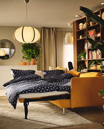 Yellow sofa bed unfolded into a bed with blue and white geometric patterned bedding under a warm pendant lamp.