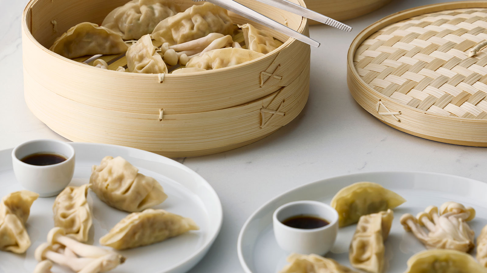 A dining setting with a bamboo KLOCKREN steamer filled with dumplings and two small bowls of dipping sauce.