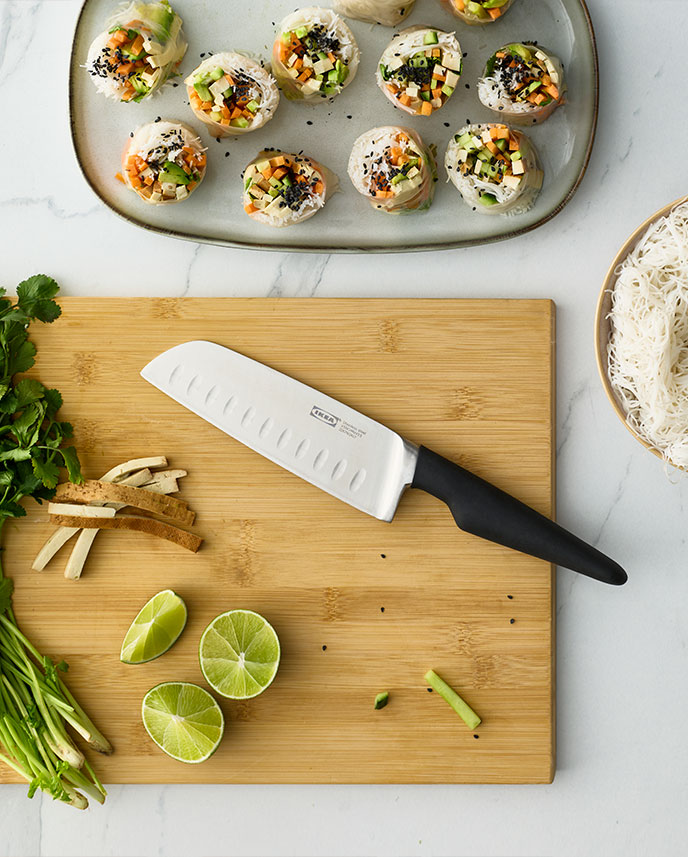 A kitchen countertop features a black VÖRDA vegetable knife alongside fresh herbs and lime, ready for meal preparation.