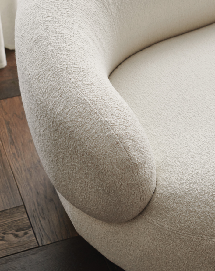Close-up of an armchair upholstered in cream-colored fabric.