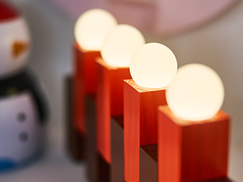 Decoración luminosa roja con esferas blancas iluminadas, colocada sobre una superficie interior. Un muñeco de nieve desenfocado aparece al fondo, creando un ambiente festivo y acogedor.