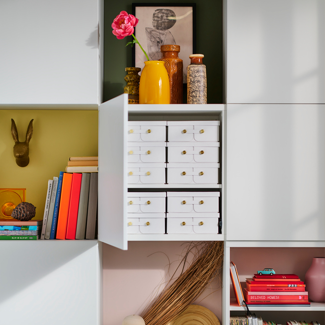 White modular storage unit with open door revealing small white organizer boxes with gold handles.