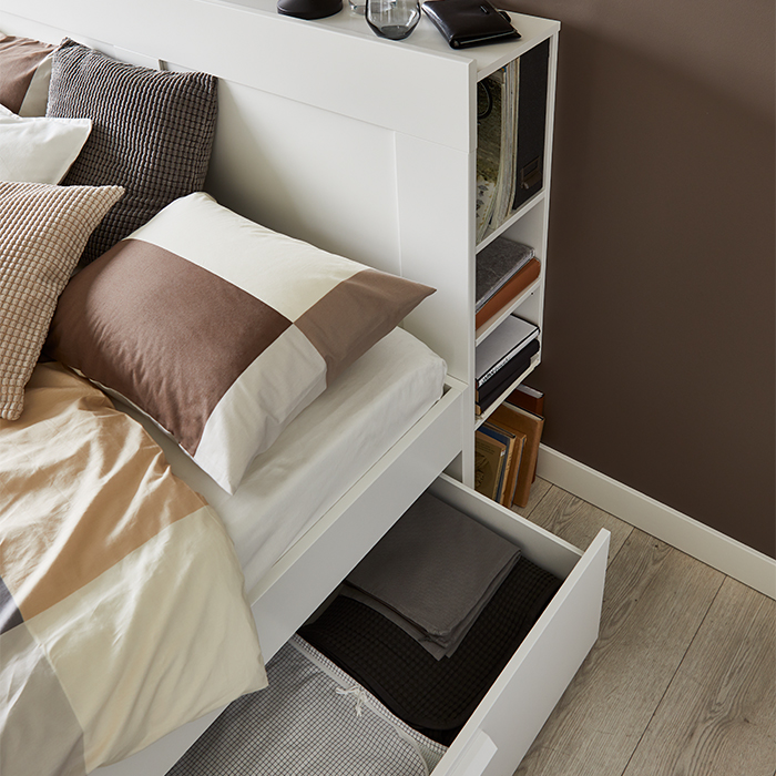 White bed featuring an open under-bed storage drawer and integrated headboard shelves.