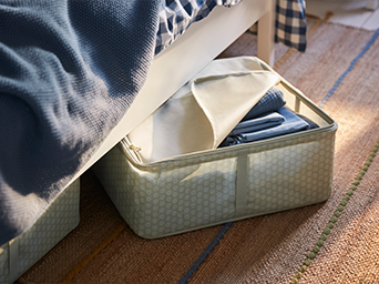 Partially unzipped fabric storage box with textiles under a wooden bed.
