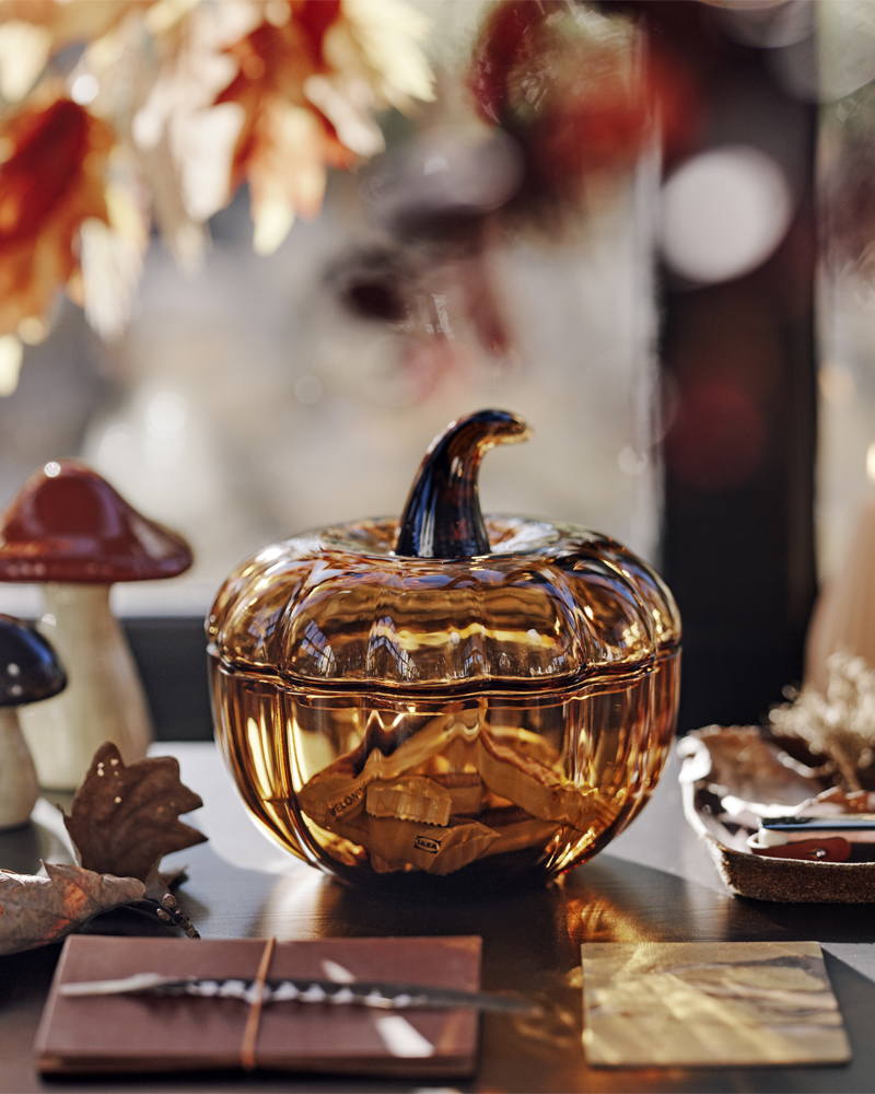 A brown HÖSTAGILLE pumpkin-shaped decoration bowl and lid filled with candy beside two HÖSTAGILLE decorative mushrooms.