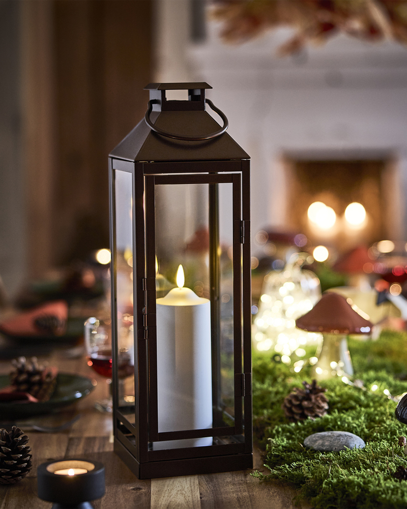 A woodland-themed table setting with a lit candle inside a lantern next to decorative mushrooms on artificial moss.