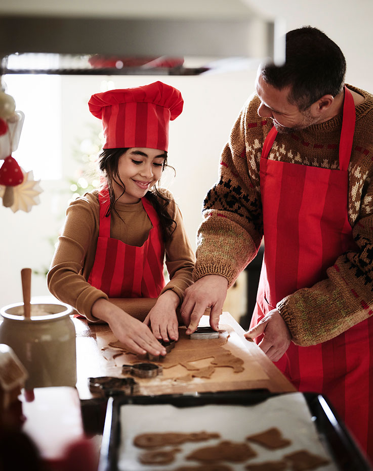 A little girl and an adult are in the kitchen baking cookies with cookie cutters on a snack table.
