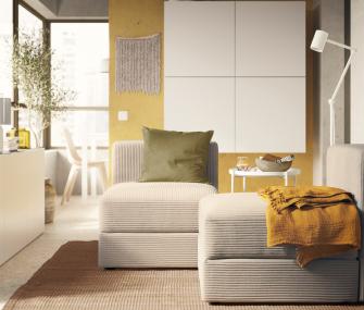 Sillón modular beis con cojín verde oliva y manta amarilla sobre alfombra marrón.