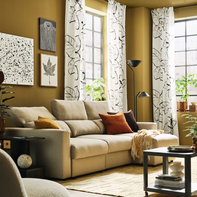 A light living room with a light-beige MALMKÖPING three seat sofa with chaise longue flanked by side tables and plants.