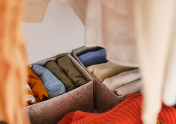Grey felt storage bins with neatly folded clothes inside a closet.