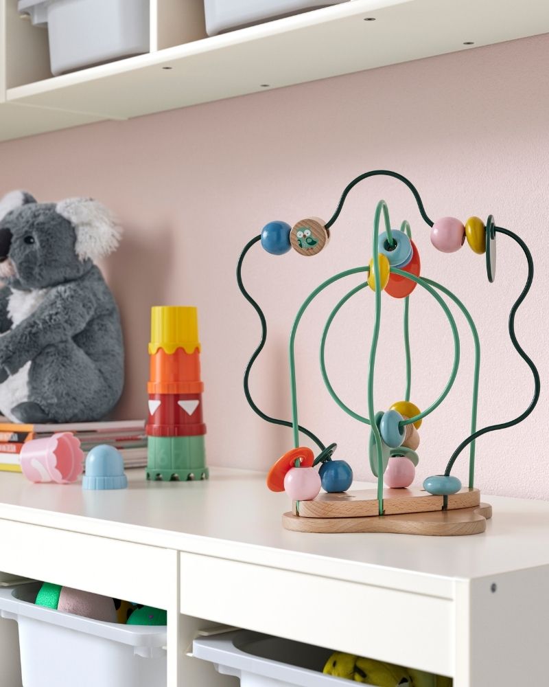 The colourful UPPSTÅ bead maze, pull toy and building beakers, all standing on top of TROFAST storage unit.