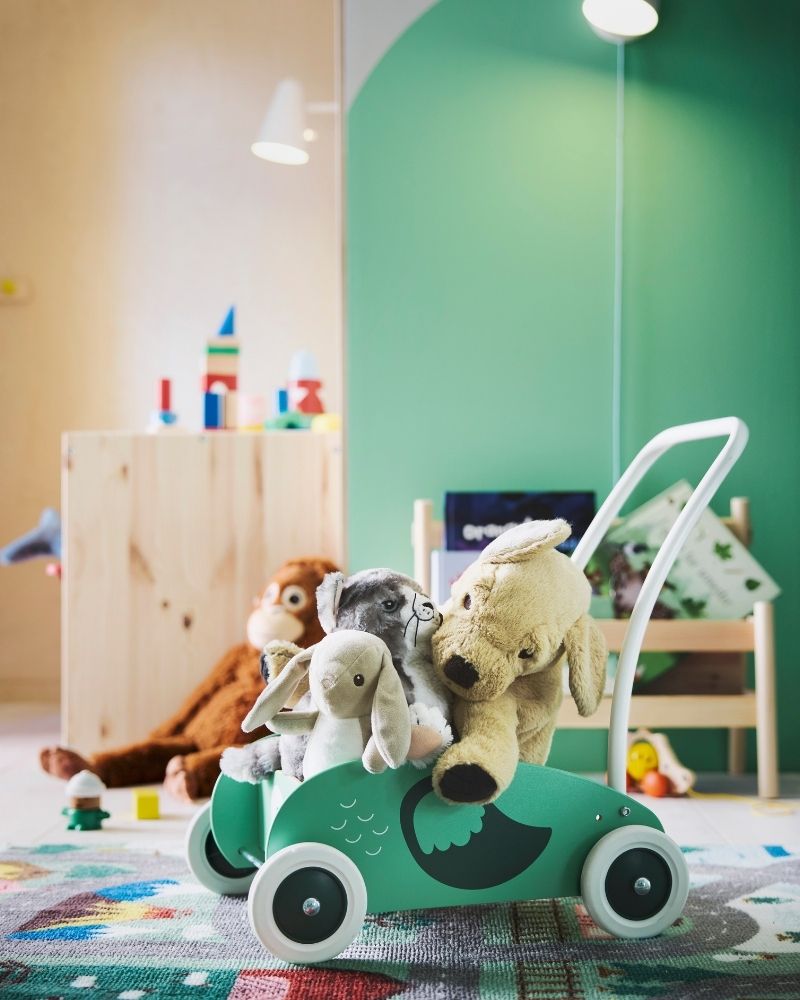 UPPSTÅ toddler walker completely full of soft toys, with a green wall behind it and the VALLABY rug underneath.
