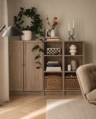 Dark wood bookcase filled with books, decorative art, and woven baskets behind a vibrant yellow sofa with cozy cushions.