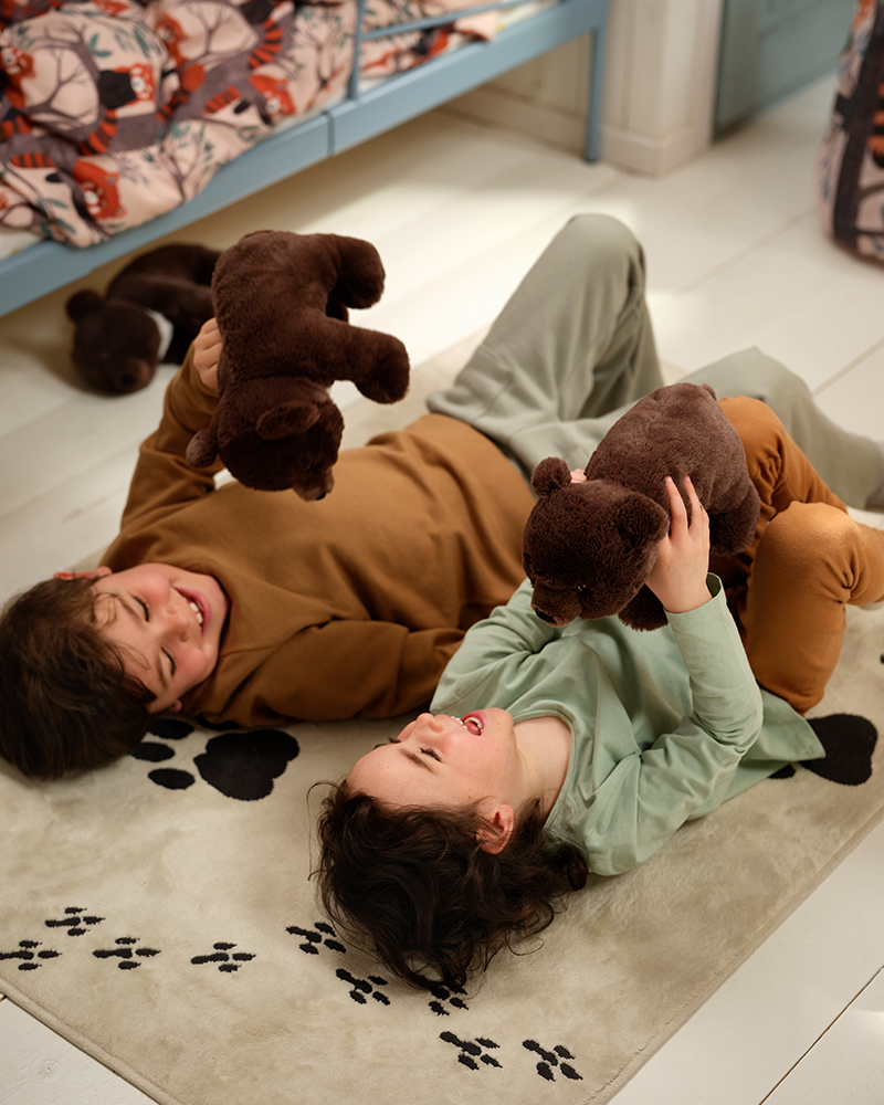 Children lying on an ALPTALL rug and playing with ALPTALL soft toy asiatic bears.