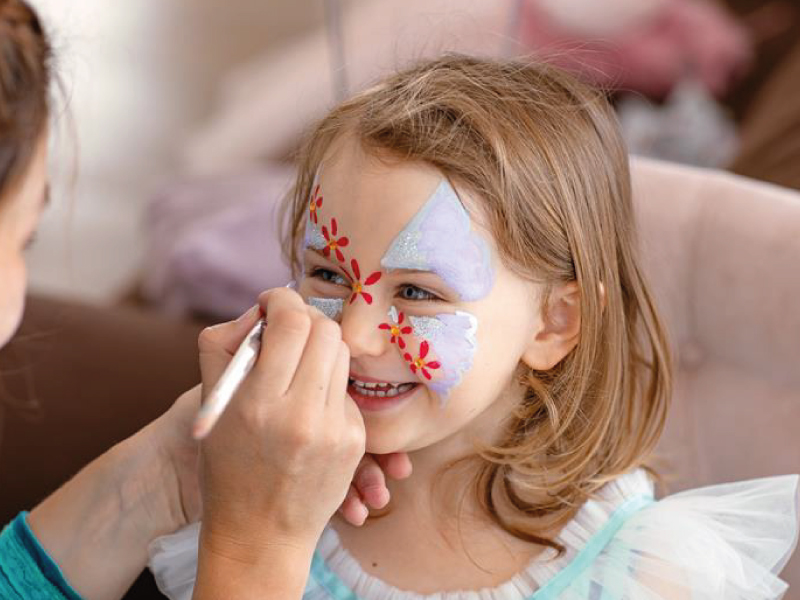 Person painting a butterfly and flower design on a child's face.