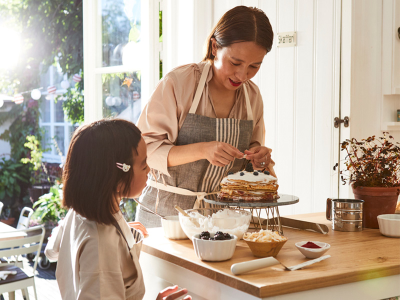 Person decorating a cake in a kitchen with help from a child.