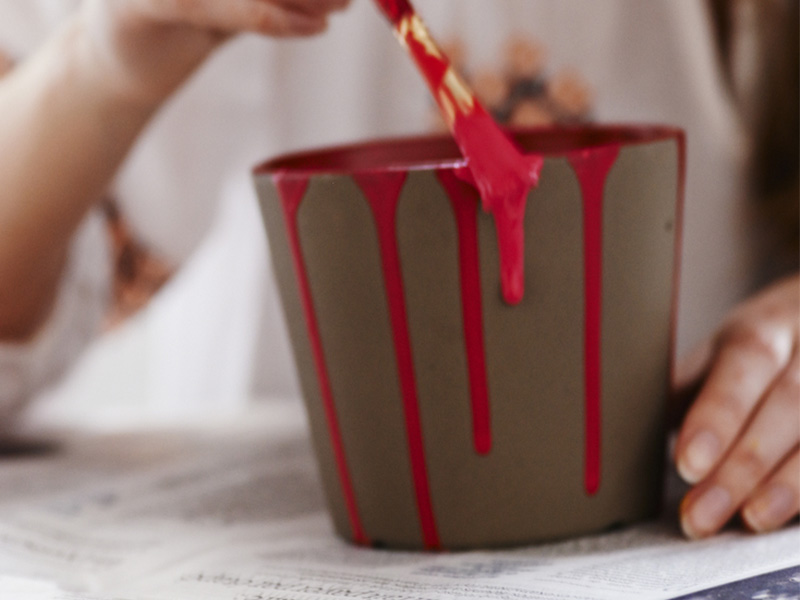 Person painting a flower pot with red paint.