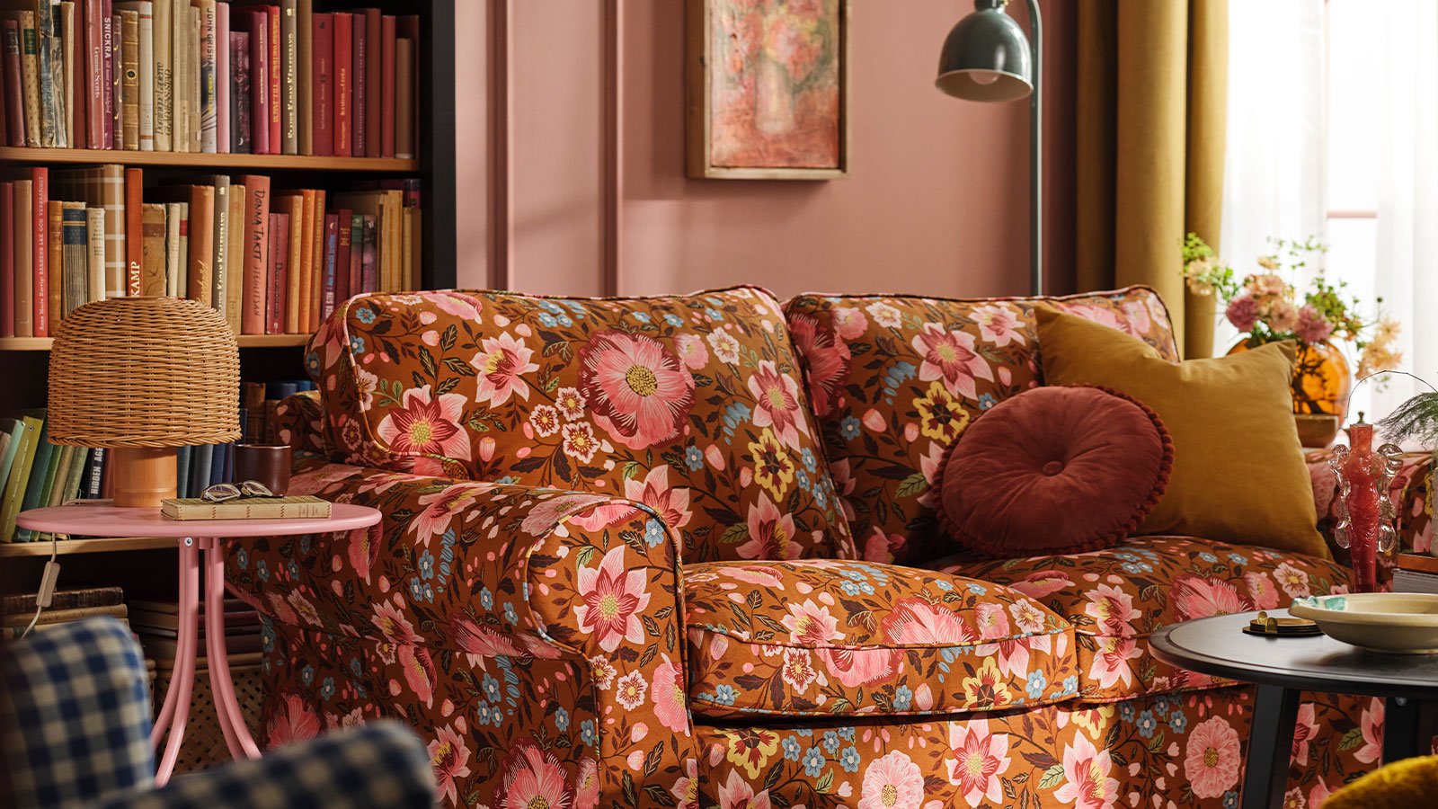 A pink living room with an EKTORP sofa dressed in a Månggbyn brown/multicoloured sofa cover in front a bookshelf.