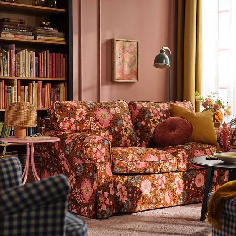 A pink living room with an EKTORP sofa dressed in a Månggbyn brown/multicoloured sofa cover in front a bookshelf.
