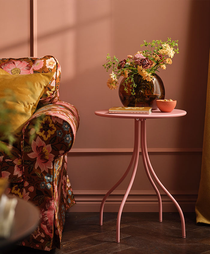Una mesita auxiliar TÅNEBRO de color rosa claro se encuentra en un salón rosa, junto a un sofá EKTORP con una funda floral.