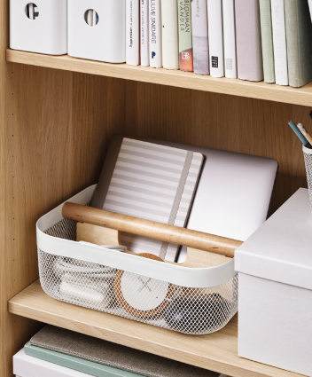 Cesta de rejilla con mango de madera organizando libreta y laptop en un estante.