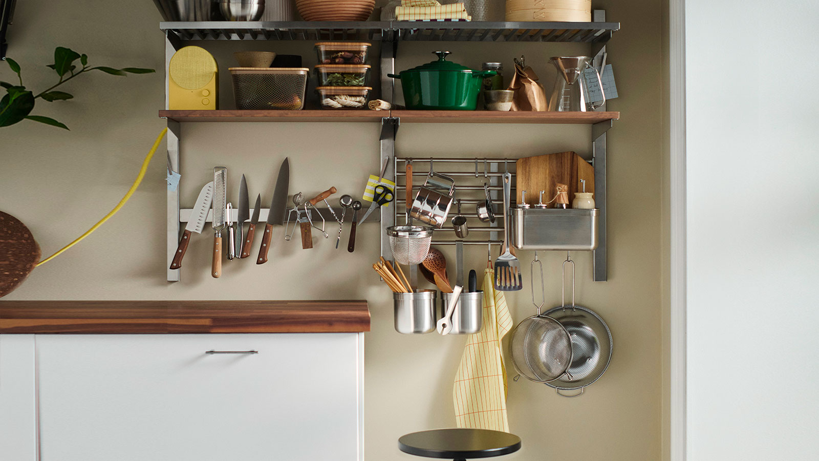 A kitchen wall fitted with open shelves, rails and a magnetic knife rack which are all packed with everyday kitchen items.
