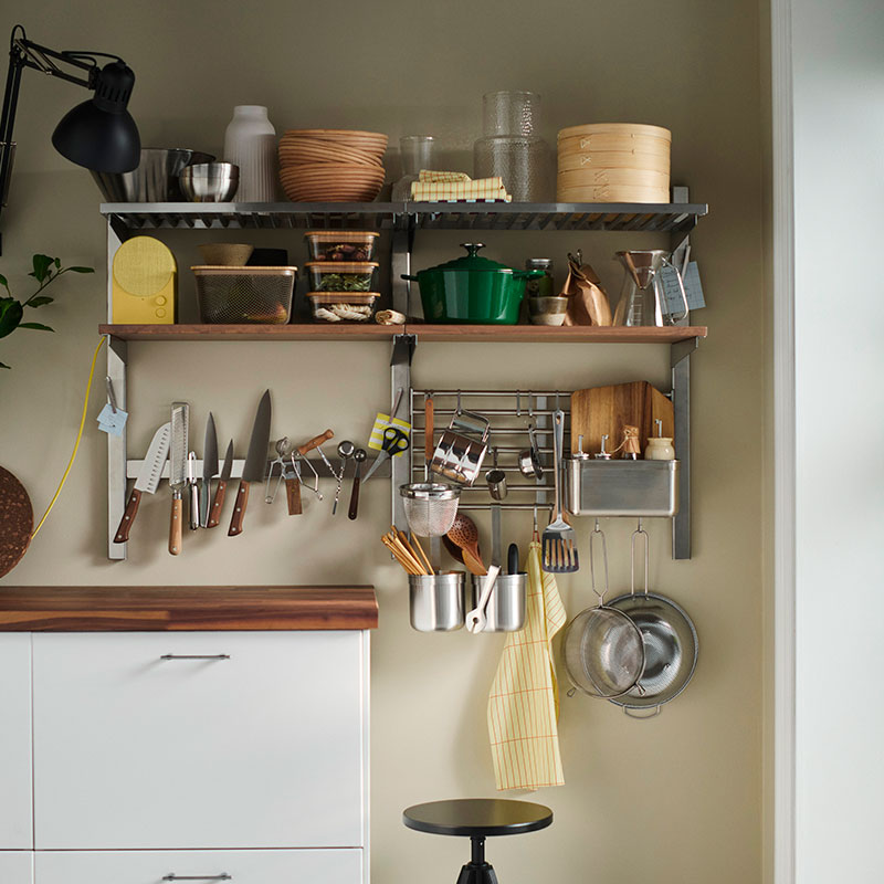 A kitchen wall fitted with open shelves, rails and a magnetic knife rack which are all packed with everyday kitchen items.