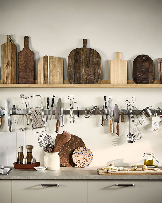 A wall with a MOSSLANDA picture ledge containing a collection of cutting boards and a KUNGSFORS magnetic knife rack.