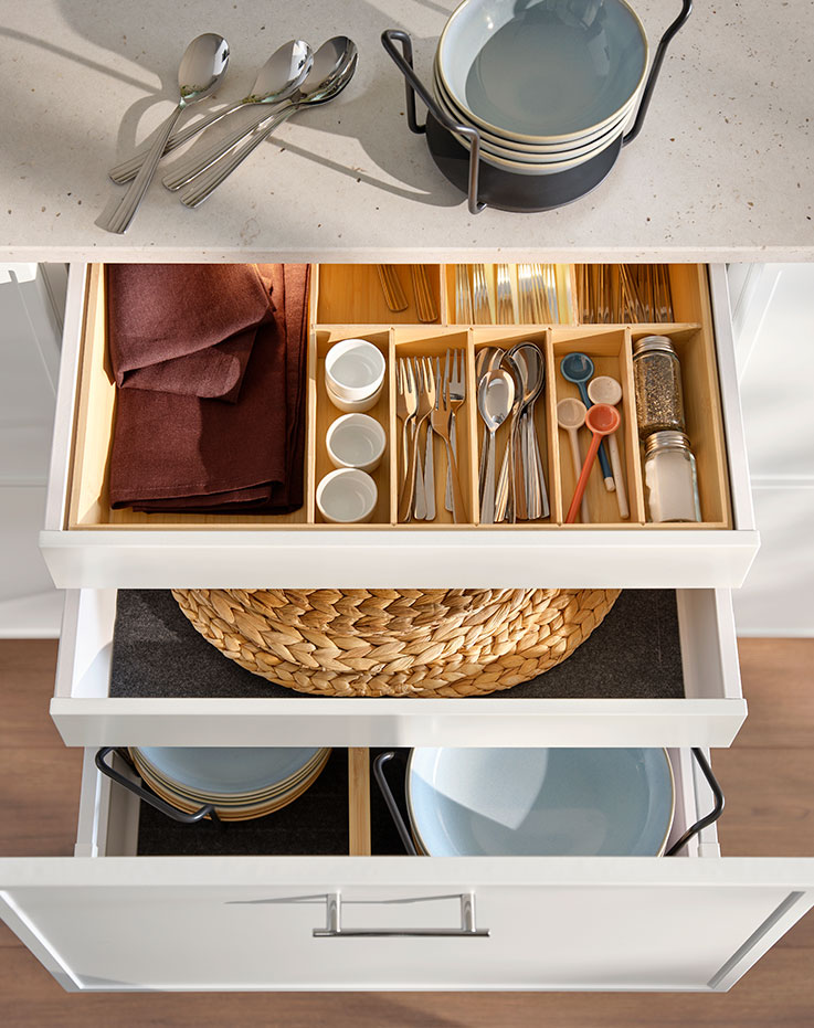 Top view of open kitchen drawers featuring an UPPDATERA bamboo cutlery tray and an UPPDATERA drawer mat and plate holder.