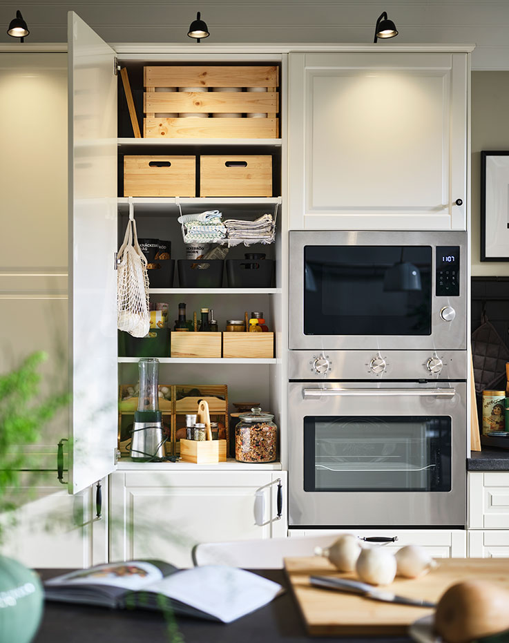 A wall of cabinets fitted with BODBYN fronts. An open door shows an organised interior lit up by TVÄRDRAG cabinet lighting.