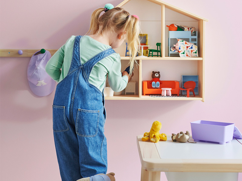 Person arranging a dollhouse in a children's room.