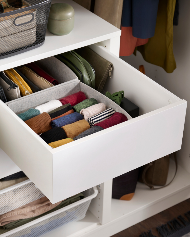 Open white drawer with neatly folded colorful socks and clothing in a modern wardrobe.