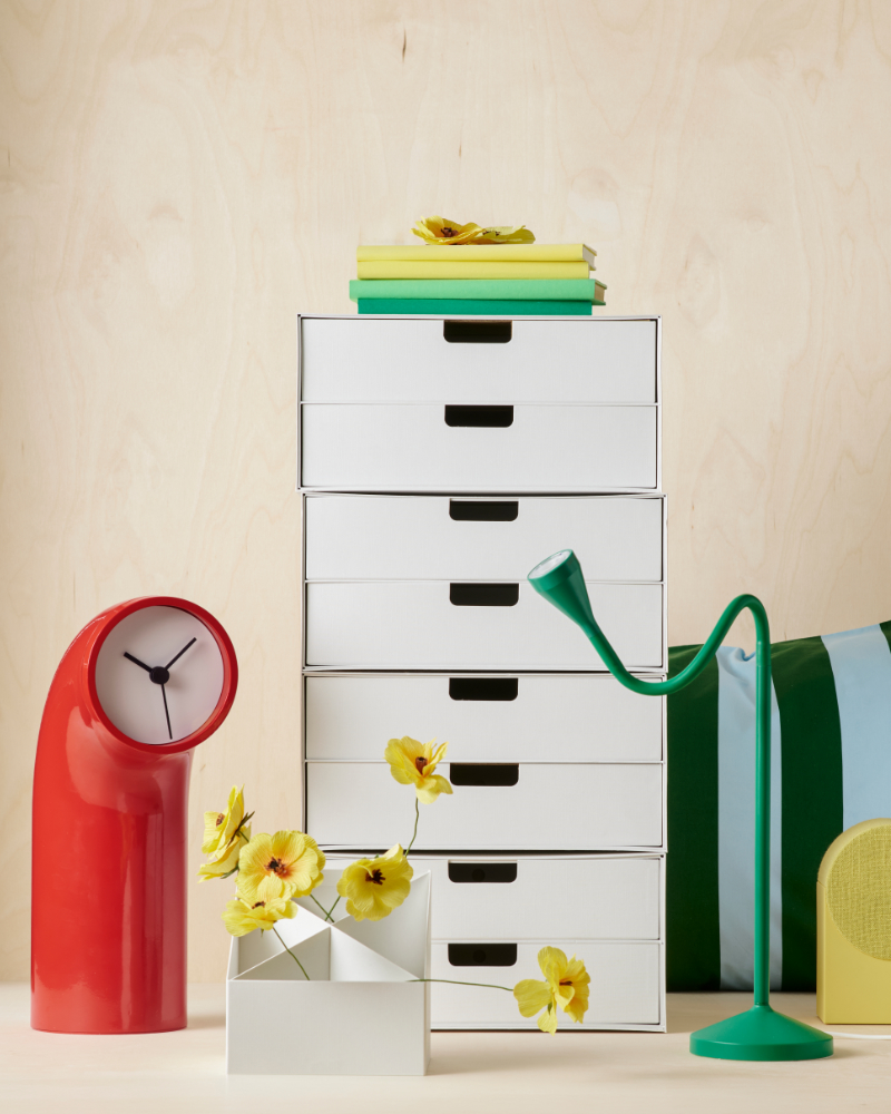 White drawer organizer with yellow flowers, red clock, green lamp, and books.