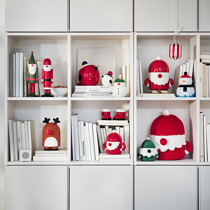Estantería blanca decorada con adornos y figuras navideñas en rojo, verde y blanco, junto a libros y peluches de Navidad.