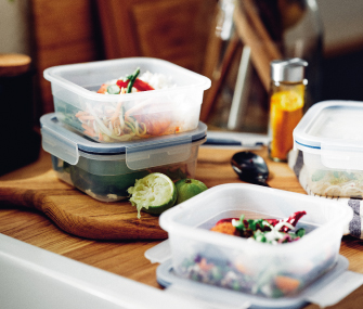 Recipientes reutilizables con ensaladas y alimentos frescos sobre una encimera de cocina.