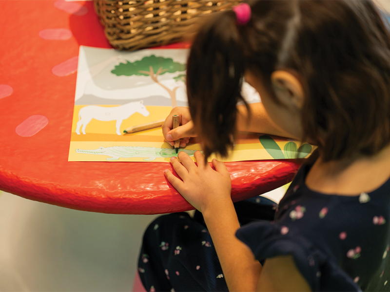 Young girl coloring an animal drawing on a red table.   