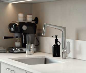 Cocina moderna con cafetera, fregadero y grifo metálico sobre una encimera blanca.