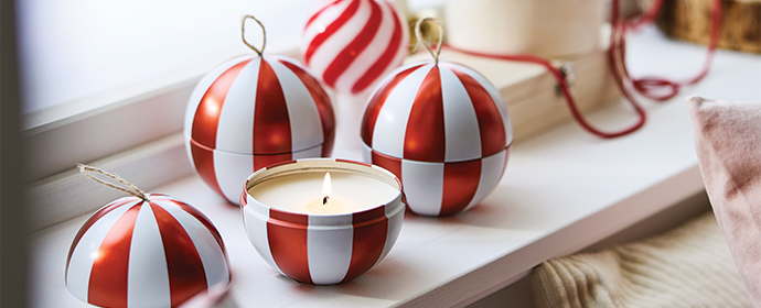 Vela encendida en contenedor con rayas rojas y blancas junto a adornos navideños.