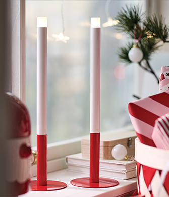 Dos velas LED delgadas en blanco y rojo sobre una repisa decorada.